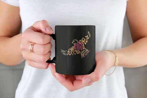 Follow Your Heart Coffee Mug Design Black mockup of a woman holding an 11 oz coffee mug