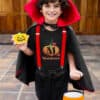 Boy standing in front of a door in Halloween costume holding a pumpkin